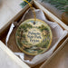 A round ornament with a scenic image of palm trees, a house, and a stream, hanging from a string.