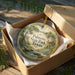 A decorative ornament in a brown box, featuring a scenic image of Palmetto State Park, Texas.