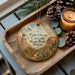 A decorative ornament with a scenic image of the Palo Duro Canyon State Park in Texas, featuring a bird and desert landscape, is displayed on a wooden tray alongside pine cones and a lit candle.