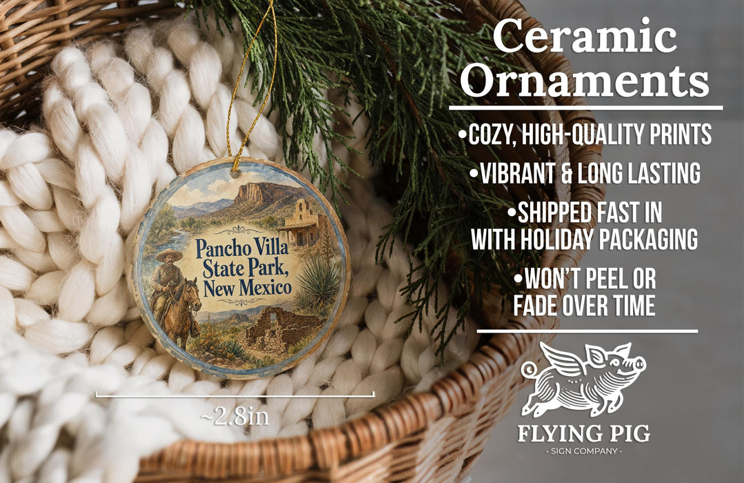 Ceramic ornaments, featuring a round ornament with a desert landscape and text, are displayed in a basket with greenery.