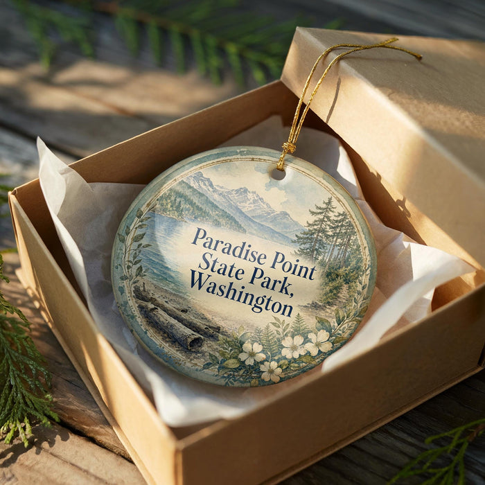 A round ornament in a box, featuring a scenic landscape of mountains, trees, and a body of water.