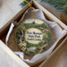 A decorative ornament in a box, featuring a scenic landscape with a waterfall, trees, and a house, with the text "Paris Mountain State Park, South Carolina" prominently displayed.