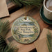 A round ornament with a scenic illustration of Pawtucket State Park, New Hampshire, hangs on a wooden surface.