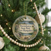A circular ornament hanging on a Christmas tree, featuring a scenic landscape with a lake, mountains, and a bird.