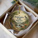 A circular ornament with a painting of a scenic landscape, featuring a waterfall and a bird, is displayed in a box.