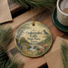A decorative ornament with a scenic image of Pedernales Falls State Park, Texas, hanging on a wooden surface.