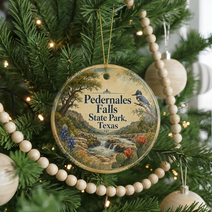 A round ornament hanging on a Christmas tree, featuring a scenic landscape with a waterfall and cactus.