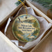 A round ornament with a scenic image of Pelican Lake, featuring a bird, a lake, and a forest, is displayed in a box.