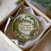 A decorative ornament in a box, featuring a scenic landscape with a lighthouse, trees, and a body of water.