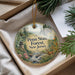 A decorative ornament with a scenic forest landscape, featuring a waterfall, pine trees, and a deer, is displayed in a box.