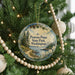 A round ornament on a Christmas tree, featuring a scenic landscape with pine trees, a lake, and mountains.