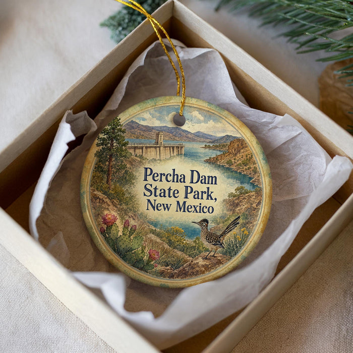 A decorative ornament in a box, featuring a bird and a scenic landscape with a bridge and mountains.
