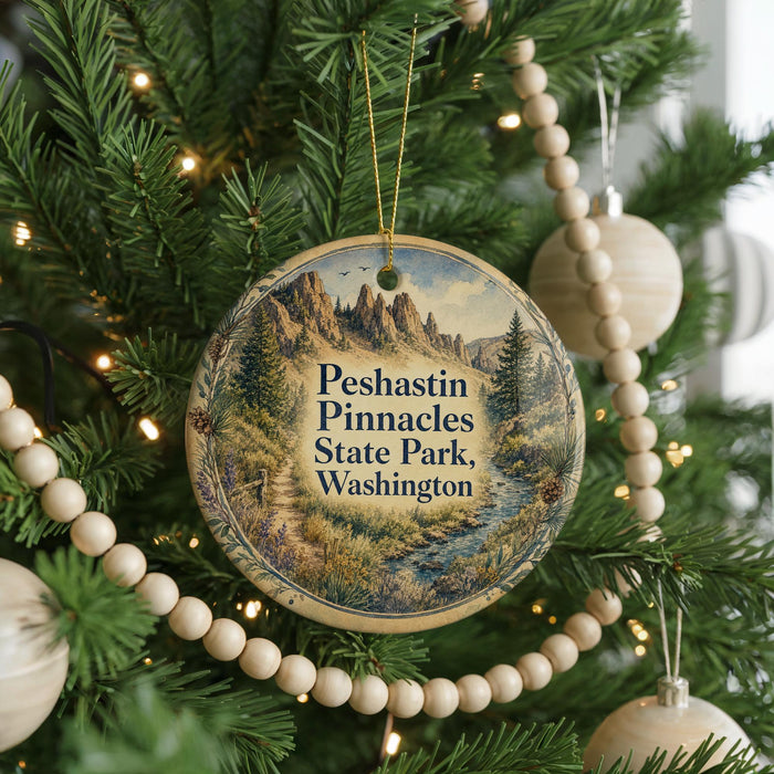 A round ornament hanging on a Christmas tree, featuring a scenic landscape with mountains and a river.