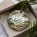 A decorative ornament with a scenic landscape of Pickwick Landing, a lake, and a cabin, hanging from a string.