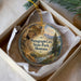 A decorative ornament in a box, featuring a scenic landscape with a cave, mountains, and a river.