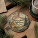 A decorative ornament featuring a scenic landscape with a river, mountains, and pine trees, hanging on a wooden surface.