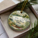A decorative ornament with a lake scene and a boat, placed in a box with pine branches.
