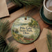 A decorative ornament featuring a scenic lake landscape with a canoe, surrounded by pine trees and a wooden dock, placed on a wooden surface alongside a cup of coffee.