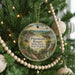 A round ornament hanging on a Christmas tree, featuring an illustration of a scenic landscape with a waterfall and a building.