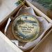 A decorative ornament in a box, featuring a scenic landscape with mountains, trees, and a lake.