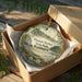 A decorative ornament in a box, featuring a scenic landscape of Pleasant Harbor State Park in Washington.