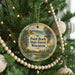 A round ornament hanging on a Christmas tree, featuring a scenic landscape with a lighthouse and a beach.