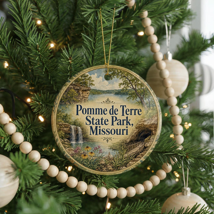 A round ornament hanging on a Christmas tree, featuring a scenic landscape with a waterfall and a bridge.