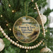 A round ornament hanging on a Christmas tree, featuring a scenic landscape with a waterfall and a bridge.