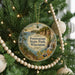 A circular ornament hanging on a Christmas tree, featuring a scenic landscape with a waterfall and a path leading to a lake.