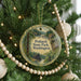 A round ornament hanging on a Christmas tree, featuring a scenic landscape with a cabin and trees.