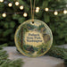 A round ornament with a painting of Potlatch State Park in Washington, surrounded by pine branches and twinkling lights.