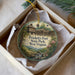 A decorative ornament in a box, featuring a painting of a historic fort surrounded by nature, with the text "Prickett's Fort State Park, West Virginia" prominently displayed.