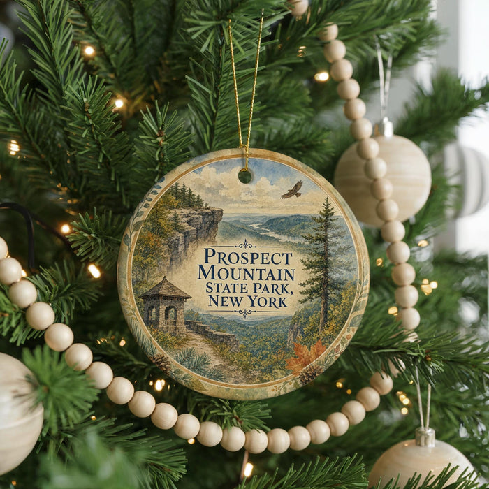 A round ornament hanging on a Christmas tree, featuring a scenic landscape with a mountain, a bridge, and a bird in flight.