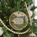 A round ornament hanging on a Christmas tree, featuring a scenic landscape with a mountain, a bridge, and a bird in flight.