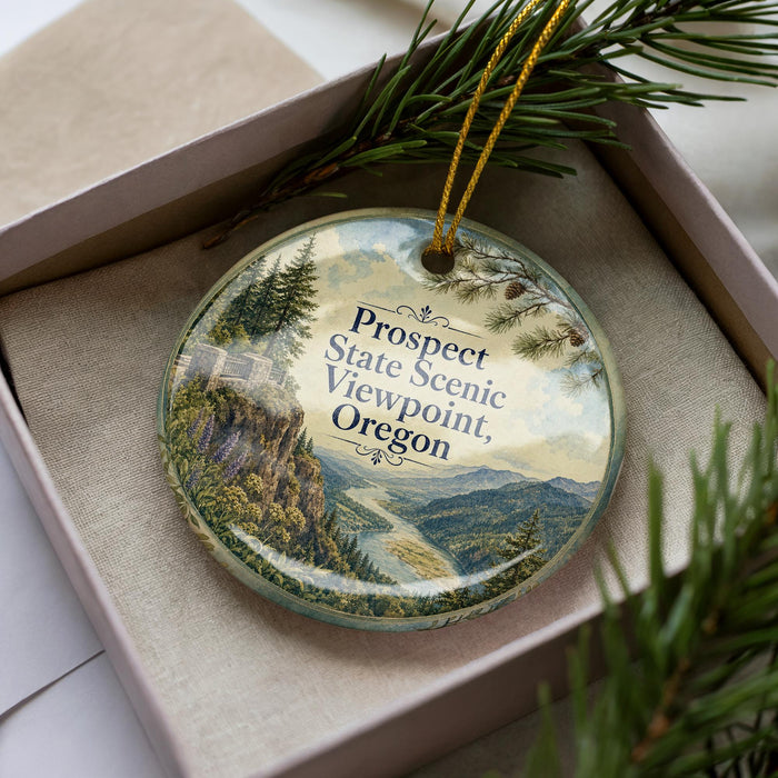 A decorative ornament in a box, featuring a scenic landscape with mountains, pine trees, and a river.