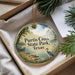 A decorative ornament with a scenic image of Purtis Creek State Park, Texas, featuring a bird and a lake, is displayed in a box with pine branches.