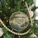 A round ornament hanging on a Christmas tree, featuring a scenic image of a lake and wildlife.