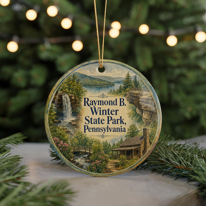 A circular ornament featuring a scenic image of Raymond B. Winter State Park, Pennsylvania, with a waterfall and a cabin in the background.