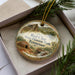 A decorative ornament in a box, featuring a scenic image of Red Clay State Historic Park in Tennessee.