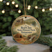 A circular ornament with a painting of a cabin and a waterfall, surrounded by greenery, hangs in front of a blurred background with twinkling lights.