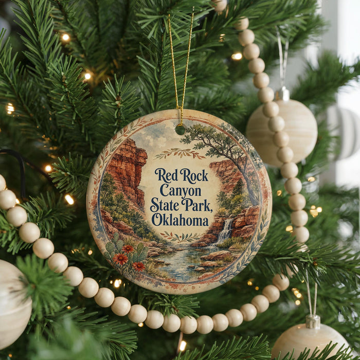 A round ornament hanging on a Christmas tree, featuring a scenic image of Red Rock Canyon State Park in Oklahoma.