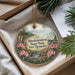 A decorative ornament with a landscape scene featuring a mountain, river, and flowers, hanging from a string.