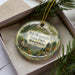 A decorative ornament in a box, featuring a scenic image of Rib Mountain State Park in Wisconsin.