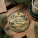 A decorative ornament with a scenic landscape of a lake, mountains, and pine trees, along with a canoe and a cabin, is displayed on a wooden surface.