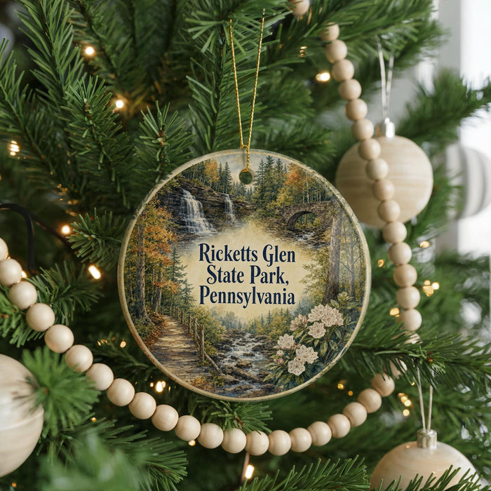 A round ornament hanging on a Christmas tree, featuring a scenic image of a waterfall surrounded by trees and a path.