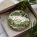 A decorative ornament in a box, featuring a scenic image of Ridley Creek State Park in Pennsylvania.