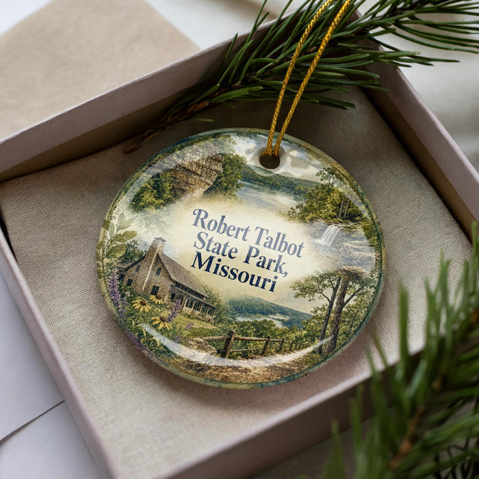 A decorative ornament in a box, featuring a scenic landscape with a house, trees, and a body of water.