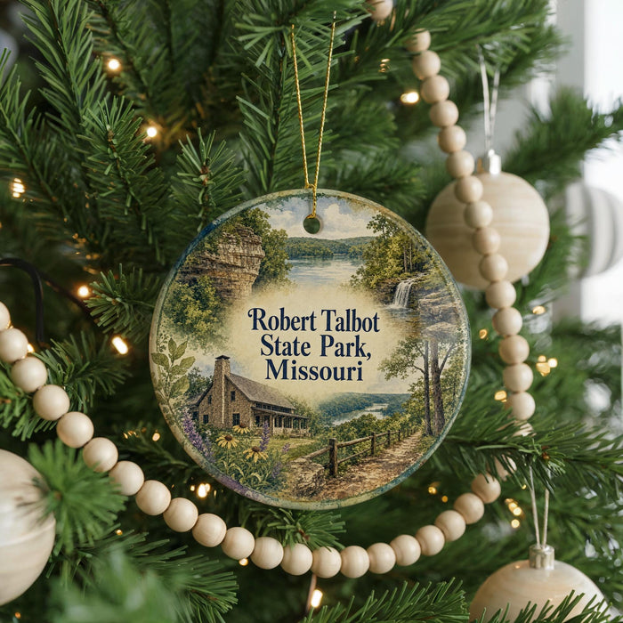 A round ornament hanging on a Christmas tree, featuring a scenic landscape with a house, trees, and a waterfall.