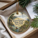 A decorative ornament with a scenic image of a park, featuring a person kayaking, a bridge, and a bird, is displayed in a box with pine branches.