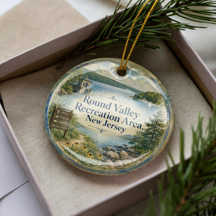 A decorative ornament in a box, featuring a scenic landscape with a lake, mountains, and a sign that reads "Round Valley Recreation Area, New Jersey".